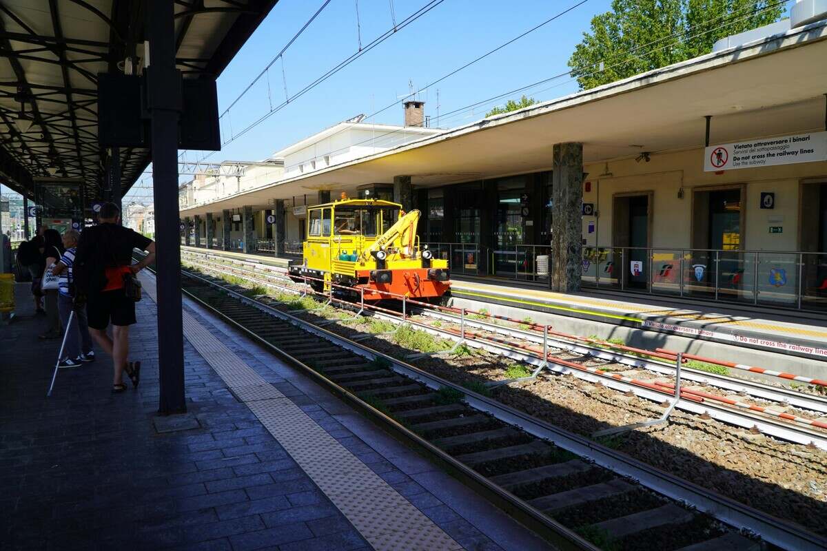 Photograph of a yellow maintenance vehicle on tracks with people waiting on the platform.