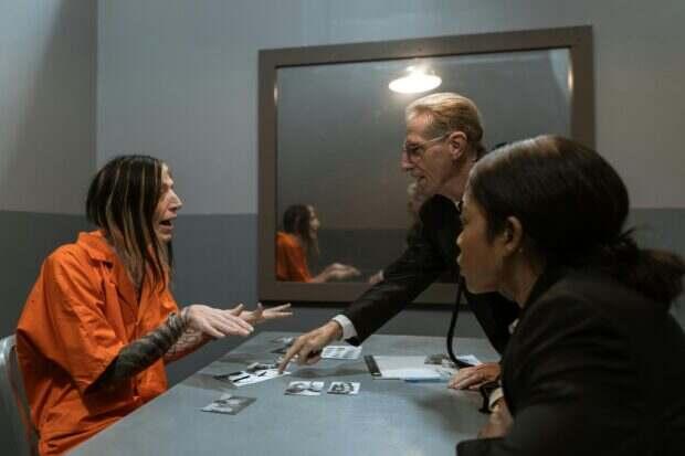 A high-intensity scene in an interrogation room with a detective questioning a handcuffed suspect.