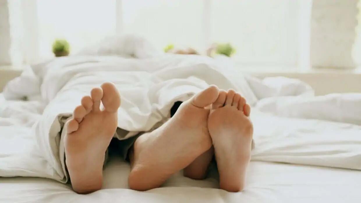 Couple's feet peeking out from under white duvet