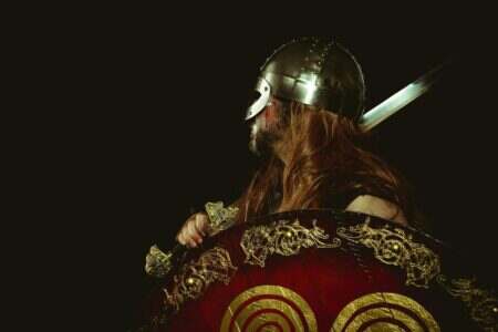 Side profile of a Viking warrior in traditional armor, holding a decorated shield and sword.