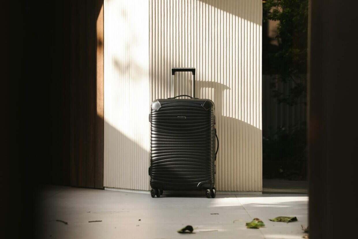 Les plus belles valises de luxe : celles qui valent vraiment chaque centime A sleek black suitcase stands in a sunlit hallway, capturing travel elegance and simplicity.