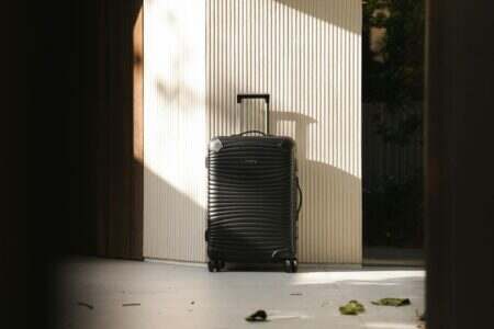 A sleek black suitcase stands in a sunlit hallway, capturing travel elegance and simplicity.