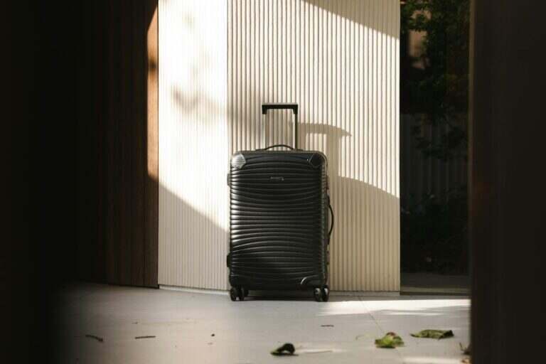 A sleek black suitcase stands in a sunlit hallway, capturing travel elegance and simplicity.