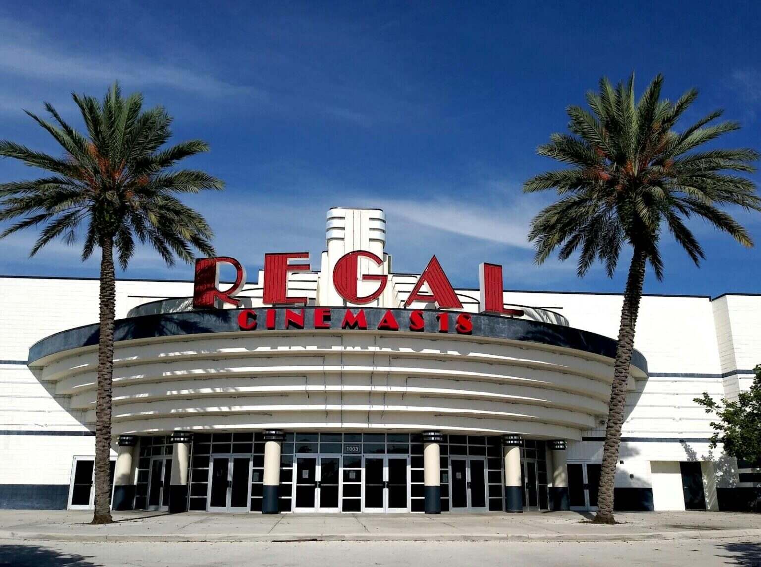 Front view of Regal Cinemas entrance with palm trees and clear sky.