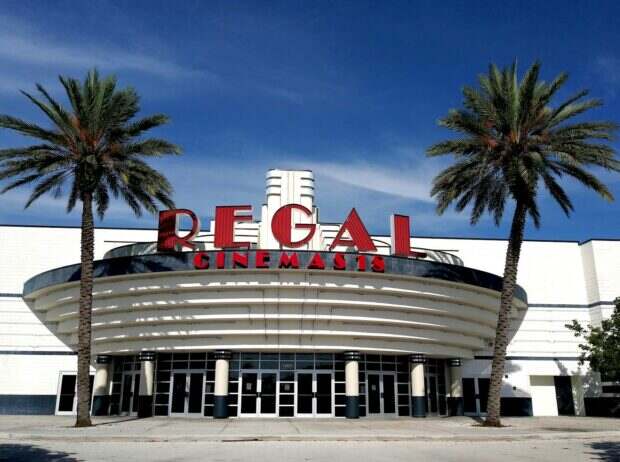 Front view of Regal Cinemas entrance with palm trees and clear sky.