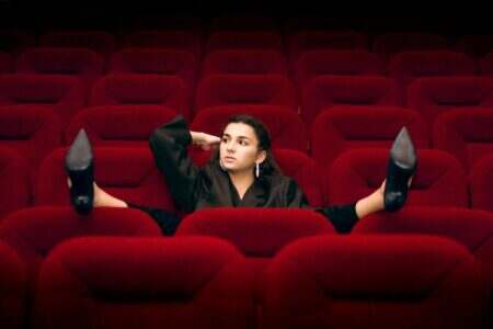 César 2026 : un jeudi sous tension, des outsiders aux crocs rayant le parquet et un Jim Carrey mystère A woman in a black blazer and high heels relaxes on red theater seats in an empty auditorium.