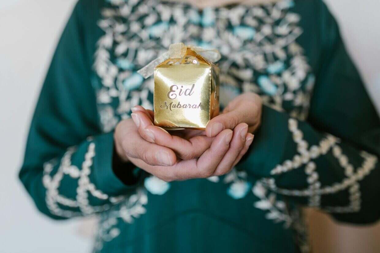 Close-up of a person holding a golden Eid Mubarak gift wrapped with a white ribbon.