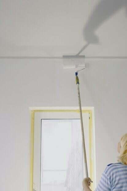 A woman paints a white ceiling using a roller in a modern apartment interior.