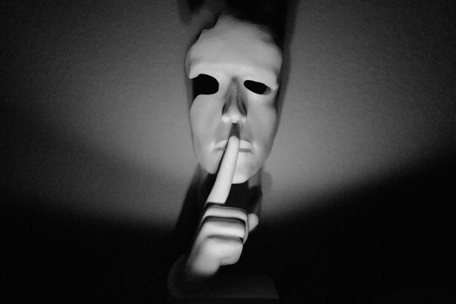 A white mask with a finger to its lips.