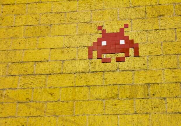 Pourquoi on ne peut pas s’empêcher de revenir aux années 2000 Street art featuring a retro pixelated space invader on a vivid yellow brick wall.