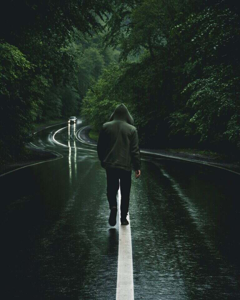 Voyager seul : quand la peur devient le plus beau des départs A solitary figure in a hoodie walks on a wet forest road, creating a mysterious and moody atmosphere.