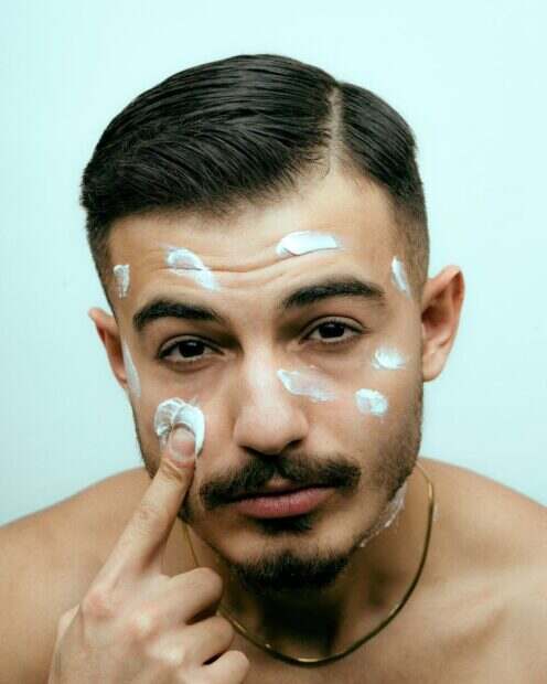 Close-up of a young man applying facial cream for skincare routine.