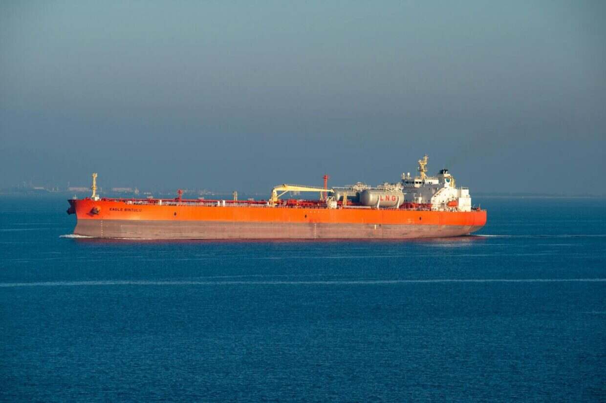 Bright orange LNG carrier ship cruising through calm sea waters on a clear day.