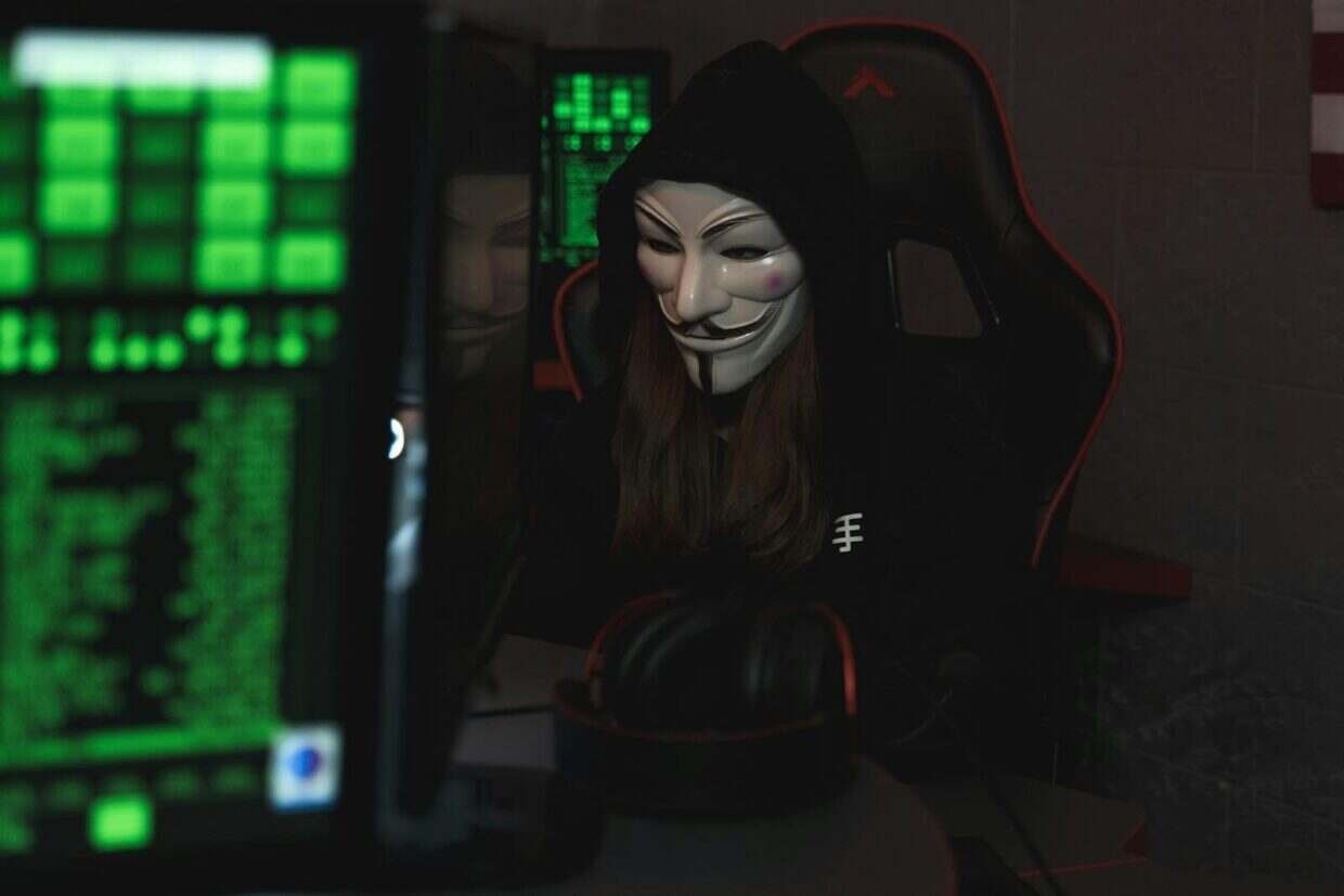 YggTorrent détruit par un hacker : la chute spectaculaire du géant français du torrent A mysterious hacker wearing a Guy Fawkes mask and black hoodie in a dimly lit room focused on computer screens.