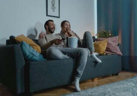 A couple relaxes indoors with popcorn, watching TV on a comfortable sofa.