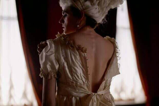 Bridgerton : la saison 4 a tout changé, la saison 5 affole déjà les fans A woman in historical attire stands with her back turned in a dimly lit room.