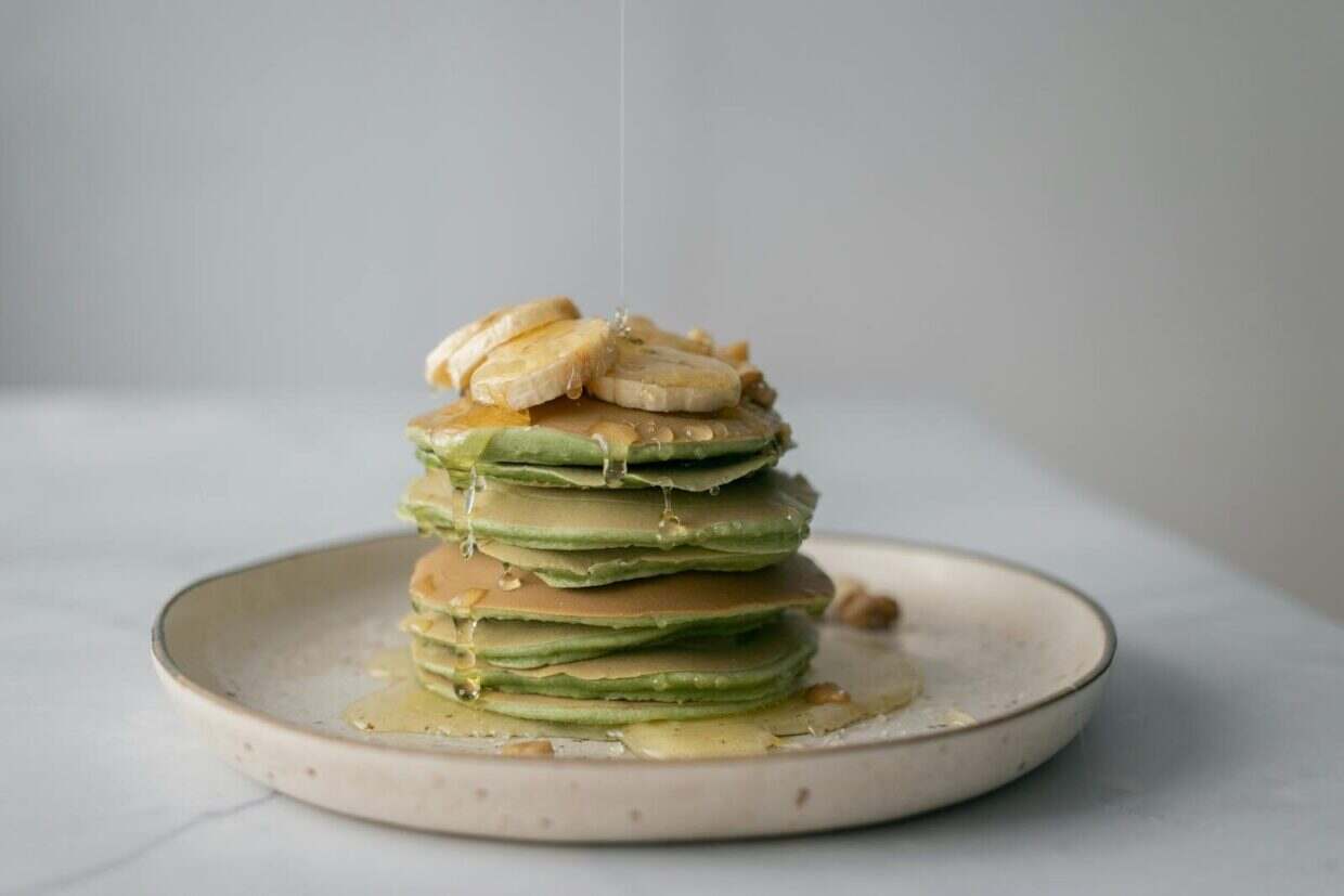 Delicious stack of green tea pancakes topped with banana slices and drizzled with honey.