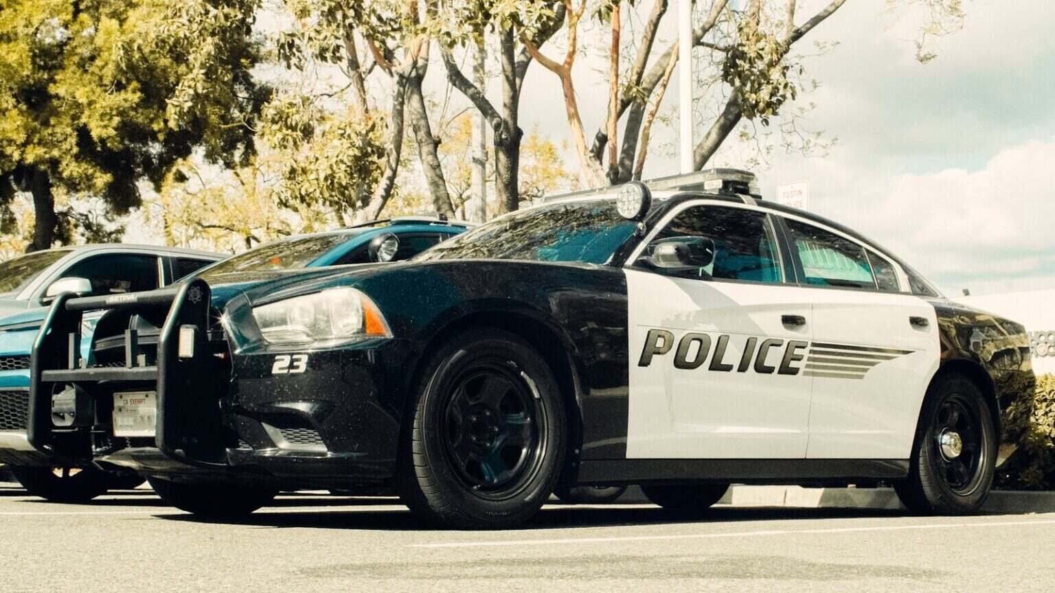 Black and white police car parked outdoors with trees in the background.