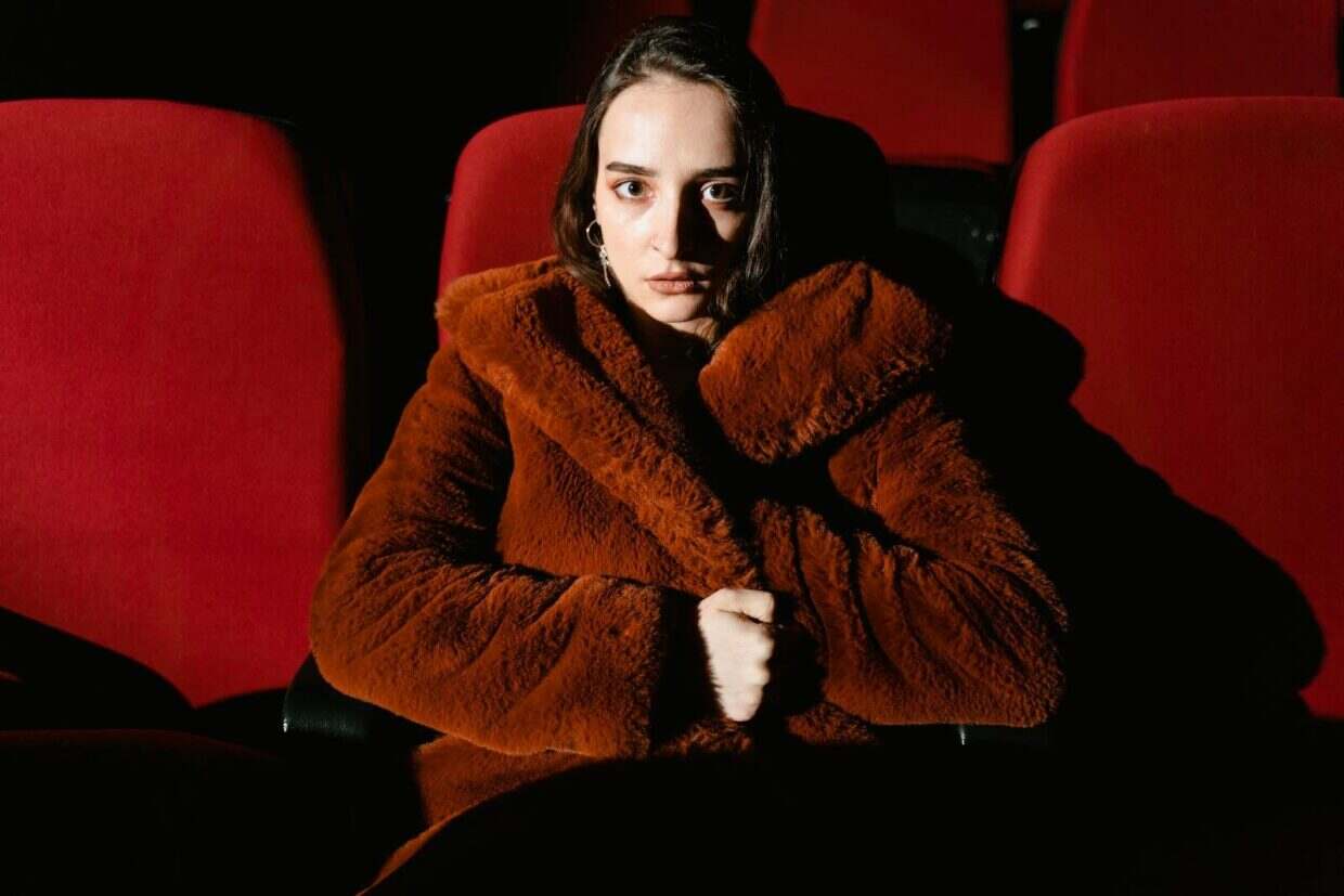 Mars 2026 : films et séries à ne pas manquer sur les plateformes de streaming et au cinéma A woman wearing a brown fur coat is sitting in a dimly lit movie theater.