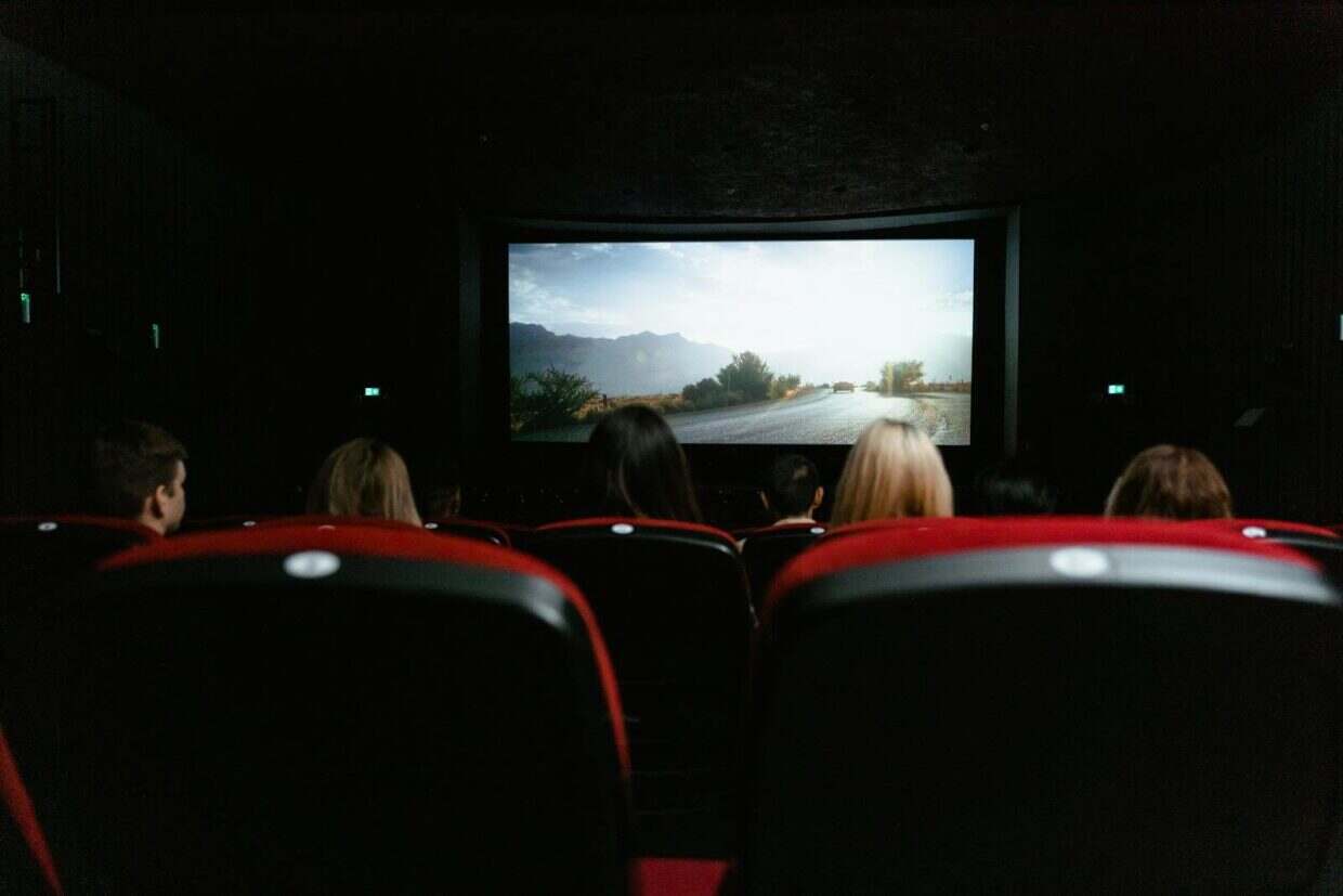 View from behind of people watching a movie in a cinema with red seats and a large screen.