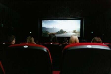 View from behind of people watching a movie in a cinema with red seats and a large screen.