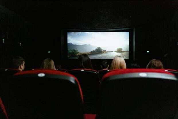 View from behind of people watching a movie in a cinema with red seats and a large screen.