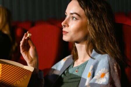 A young woman enjoys popcorn while watching a movie in a cinema theater.