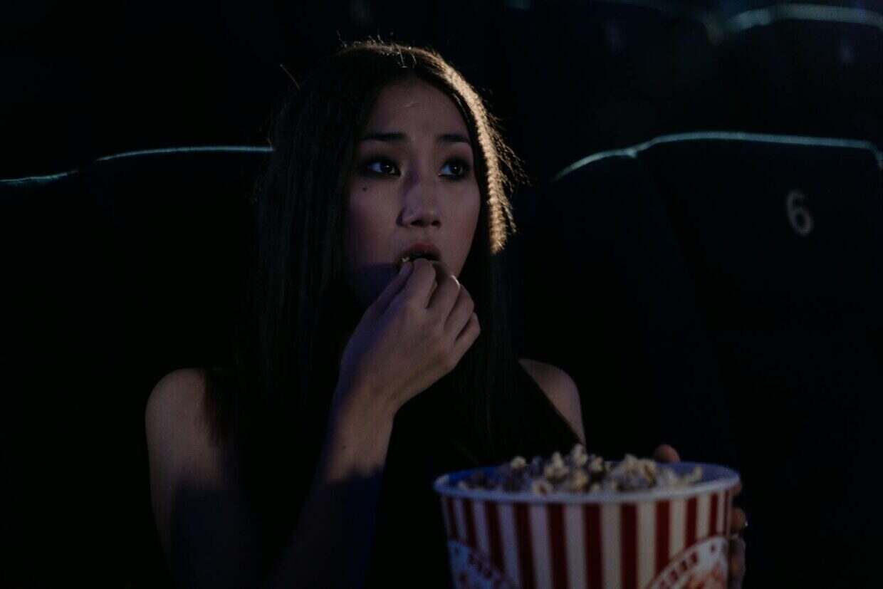 An East Asian woman enjoying popcorn while watching a movie in a theater.