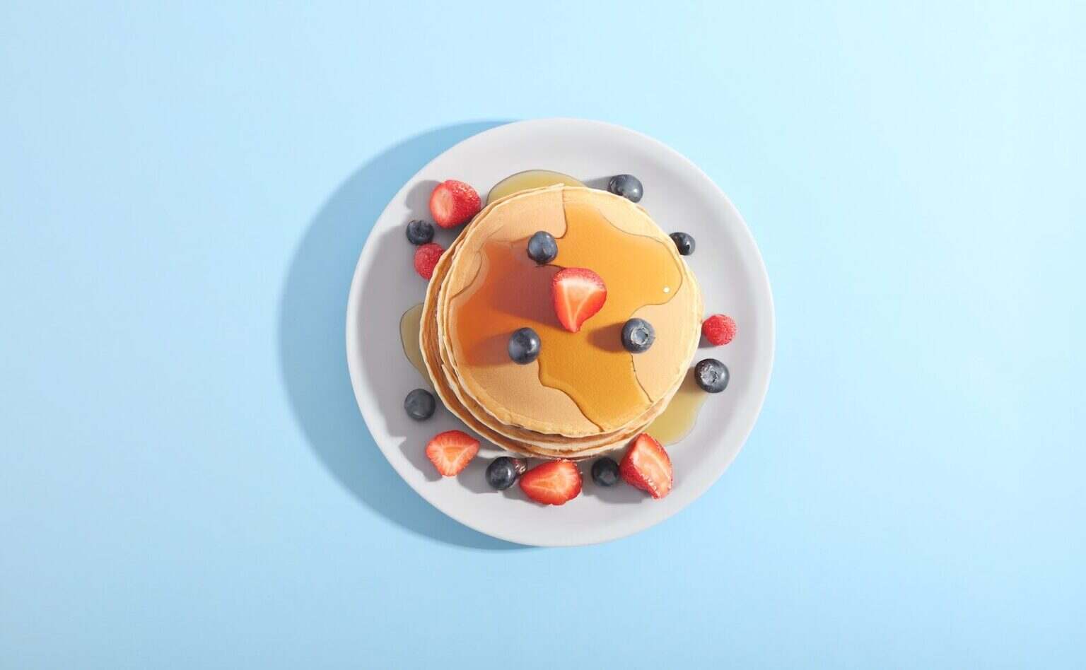 Pancakes : recettes avec une authentique recette américaine , astuces et histoire Pancakes with berries and syrup on a plate.