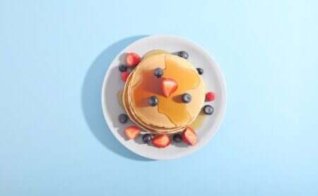 Pancakes : recettes avec une authentique recette américaine , astuces et histoire Pancakes with berries and syrup on a plate.