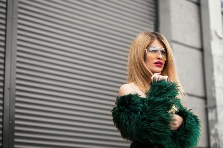 Stylish woman in green faux fur and sunglasses posing against urban backdrop.