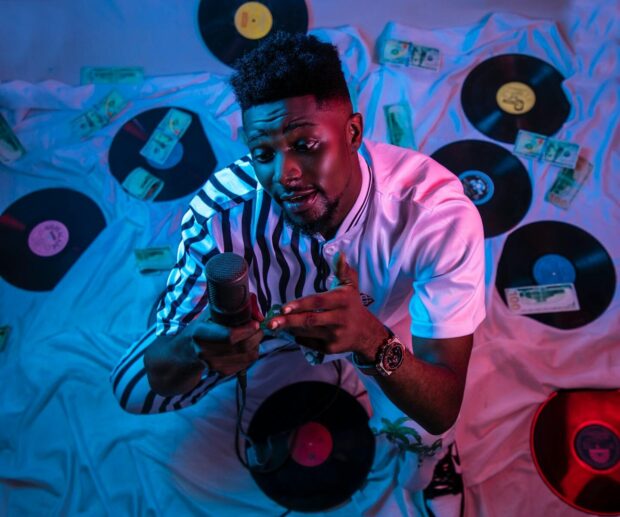 High-angle photo of an African man holding a microphone surrounded by vinyl records and dollar bills.