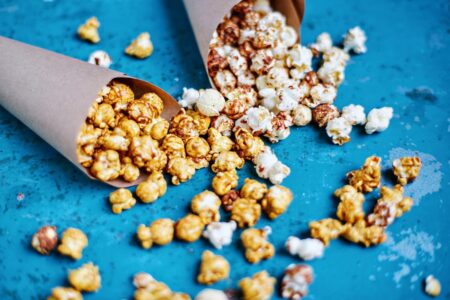 Delicious caramel and plain popcorn spilling from paper cones onto a vibrant blue surface.