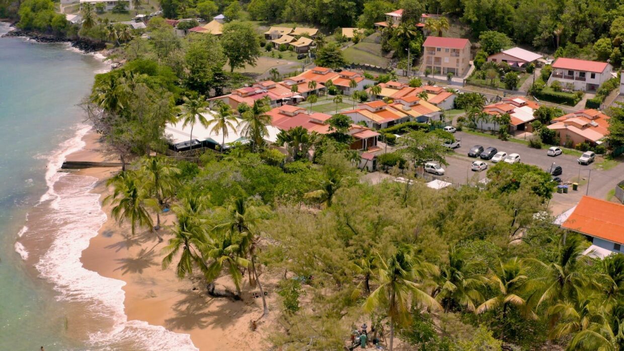 Aerial view of a tropical beachfront community with lush greenery and vibrant rooftops.