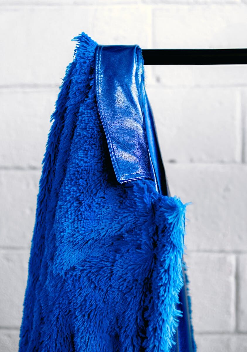 Vibrant blue faux fur coat hanging stylishly on a rack against a neutral wall.