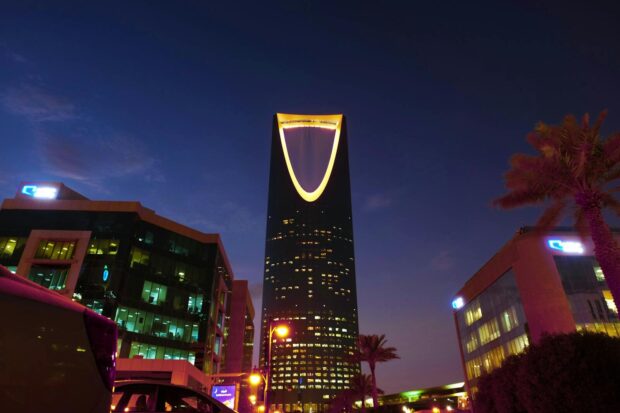 Illuminated Kingdom Centre Tower rises in Riyadh's urban landscape at twilight.