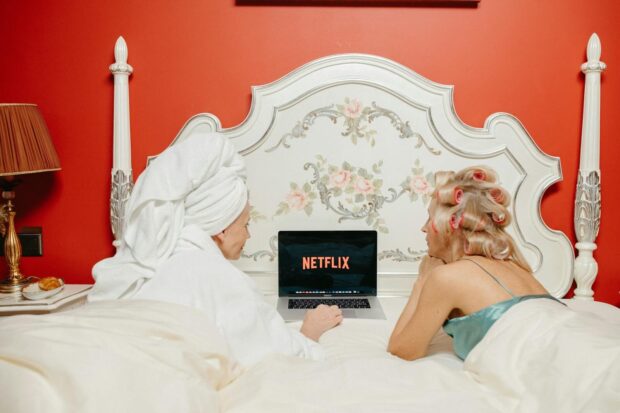Two women lying in bed watching Netflix on a laptop, creating a cozy and bonding atmosphere.