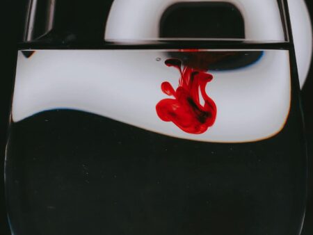 Drop of red paint dripped into transparent crystal class of water in black studio