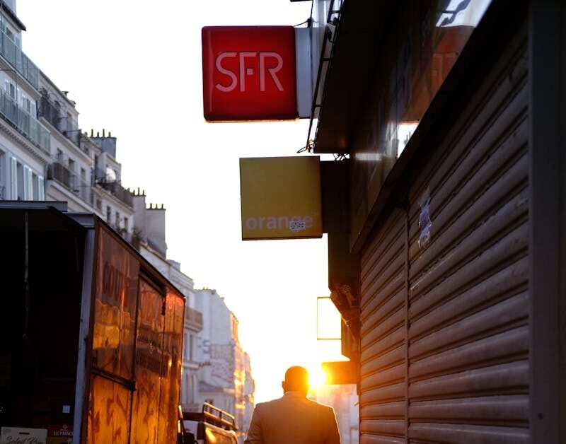A silhouette of a man walking down a Parisian street during sunset, casting long shadows.