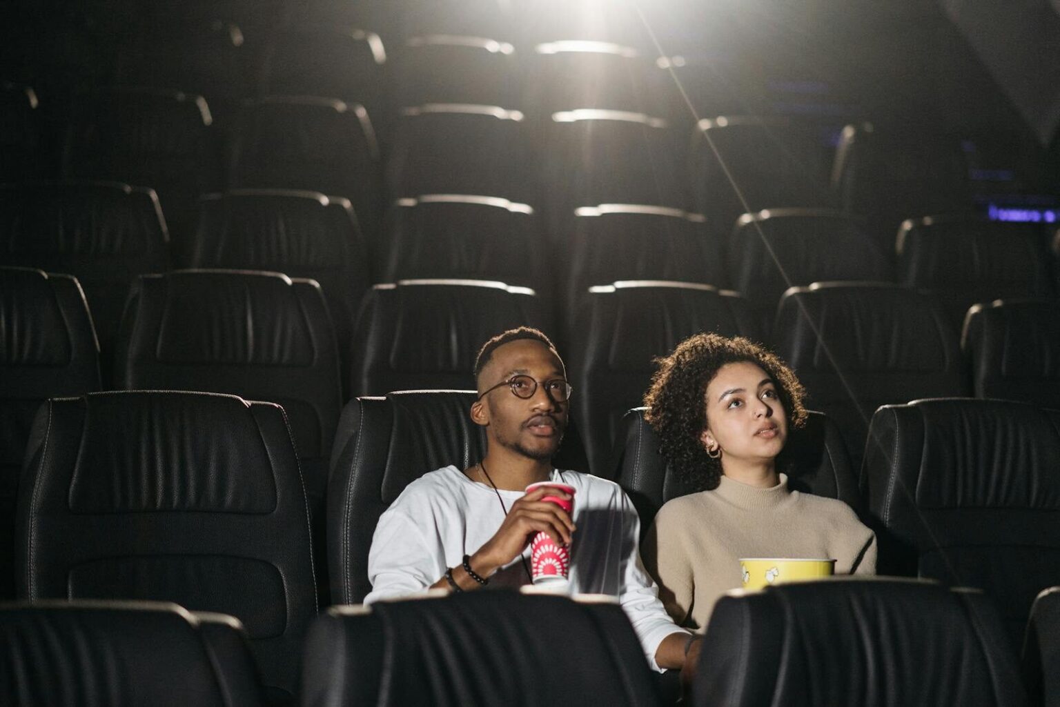 A couple seated in a movie theater enjoying a film together with snacks.