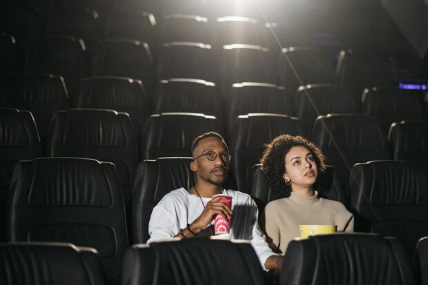 A couple seated in a movie theater enjoying a film together with snacks.
