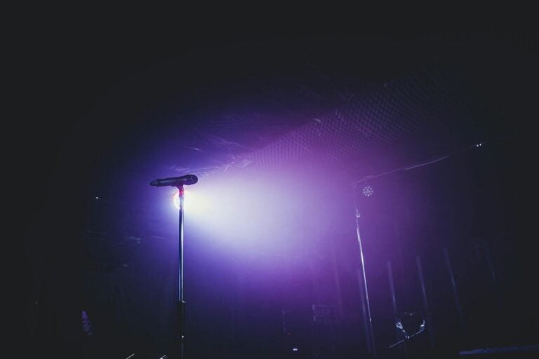 A moody stage setup with a microphone under purple lighting, perfect for concerts.