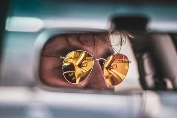 Close-up of a person's sunglasses reflecting a scenic drive viewed from a rear view mirror.