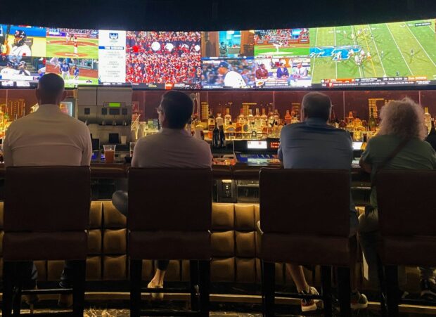 Comment les bookmakers calculent les cotes des paris sportifs : marge, probabilités et algorithmes expliqués a group of people sitting at a bar watching tv