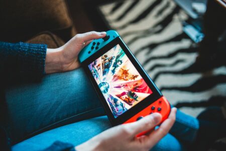 Person gaming on a handheld Nintendo Switch console with blurred background.