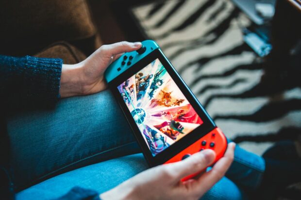 Person gaming on a handheld Nintendo Switch console with blurred background.