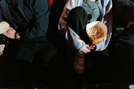 A couple sitting indoors at a movie theater, sharing a box of popcorn.