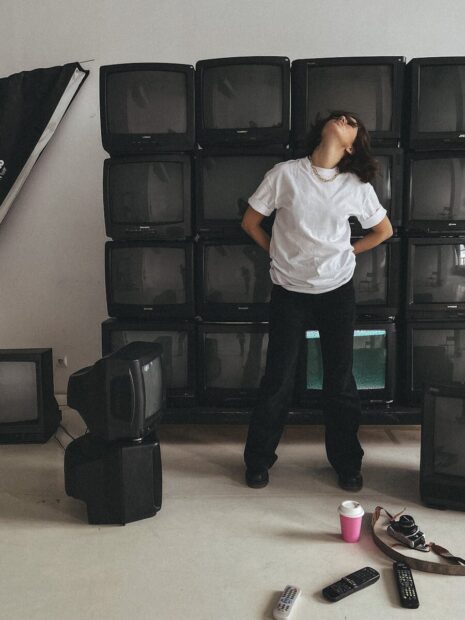 A person poses in an artistic studio filled with vintage TVs, creating a retro-modern vibe.