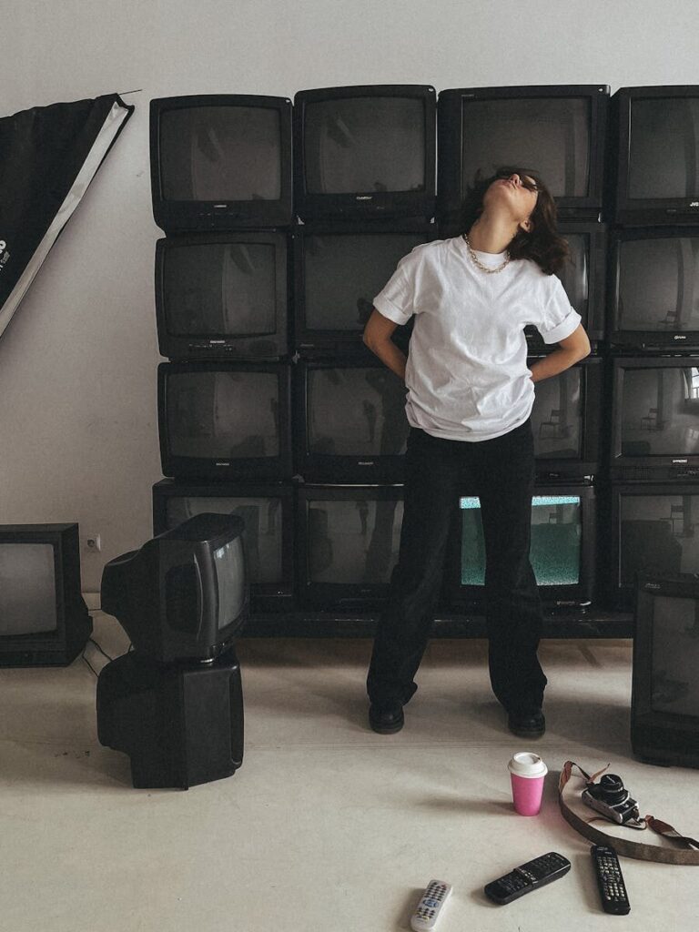 A person poses in an artistic studio filled with vintage TVs, creating a retro-modern vibe.