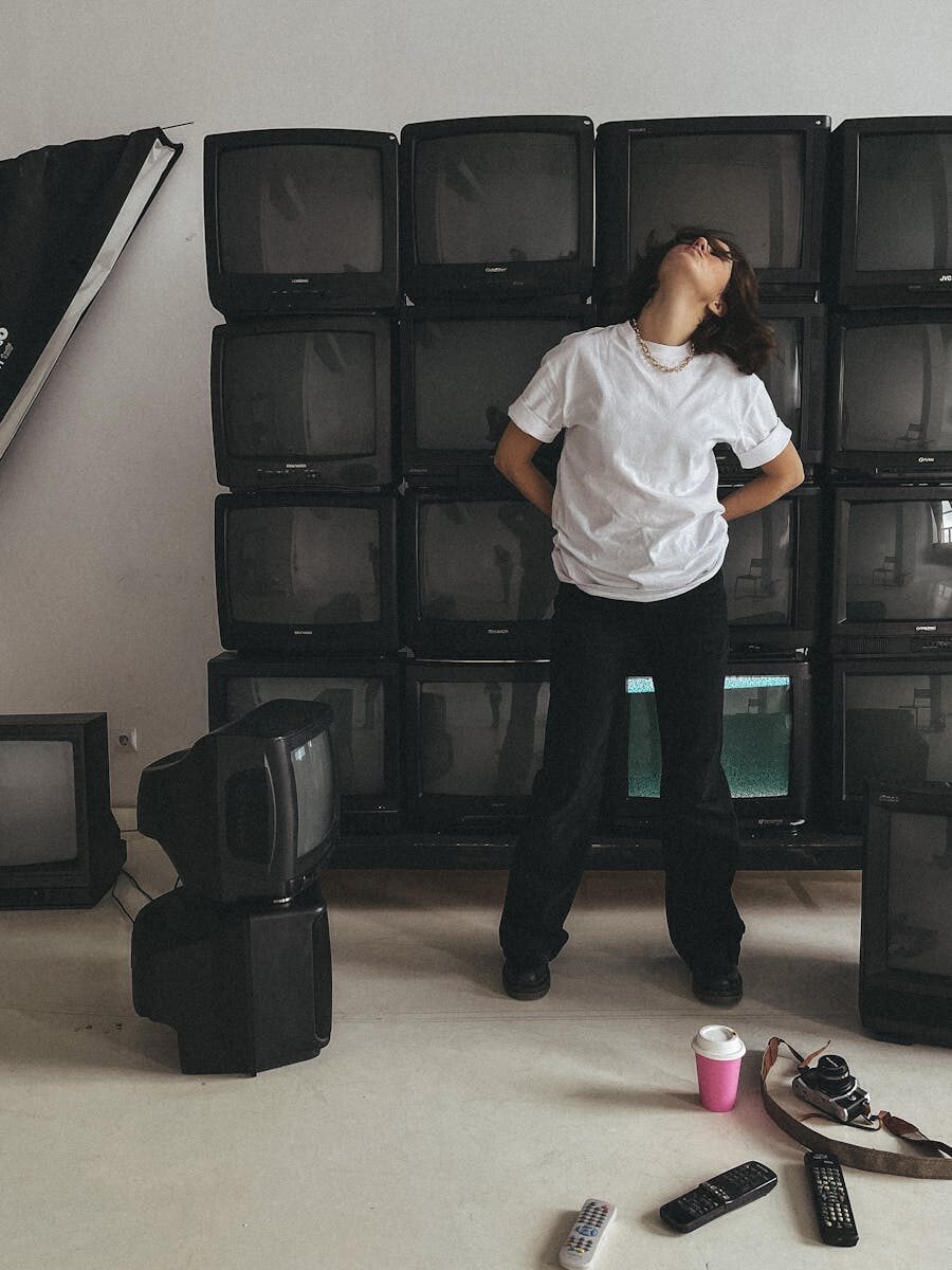 Quelle télé pour vraiment voir les films comme il faut : notre sélection sans pitié A person poses in an artistic studio filled with vintage TVs, creating a retro-modern vibe.